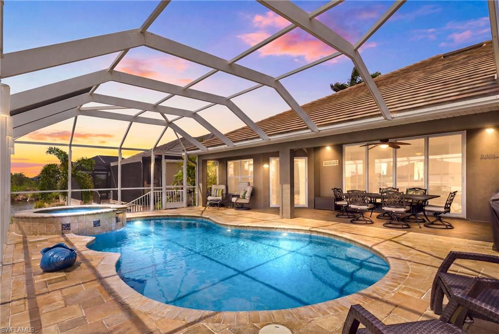 Screened lanai featuring a freeform pool, integrated spa with tile accents, and paver decking