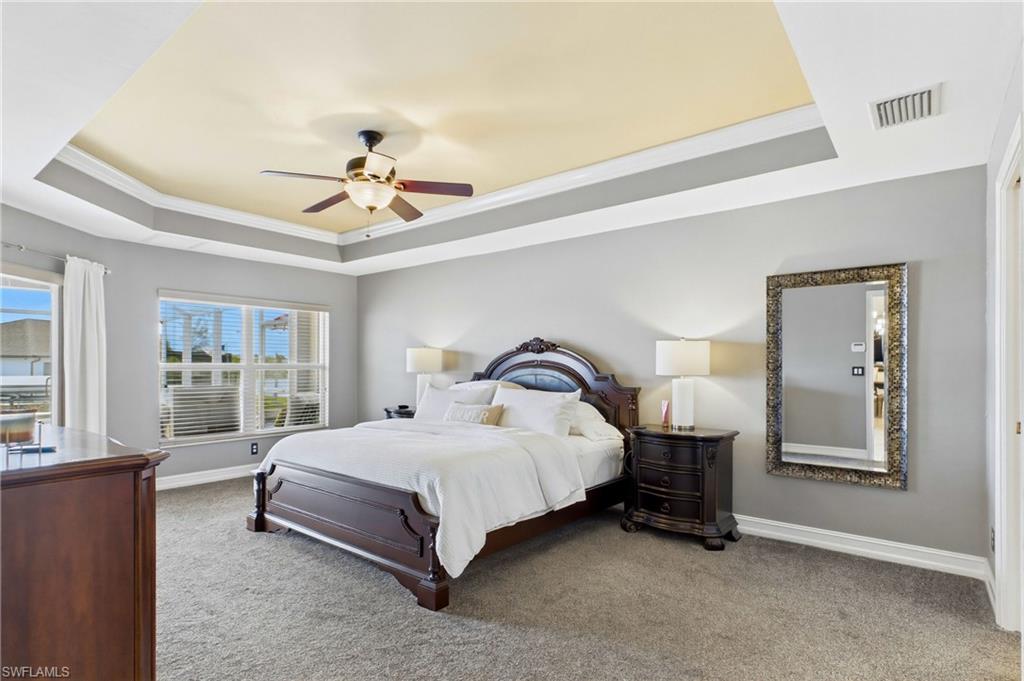 Carpeted interior space featuring a multi-tiered tray ceiling, ceiling fan with light fixture, and multiple windows