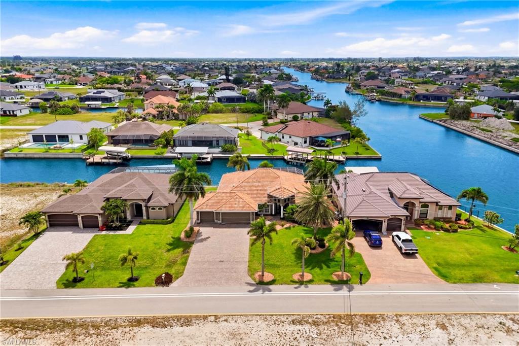 Waterfront property featuring a well-maintained lawn, mature palm trees, an attached garage, and a concrete driveway