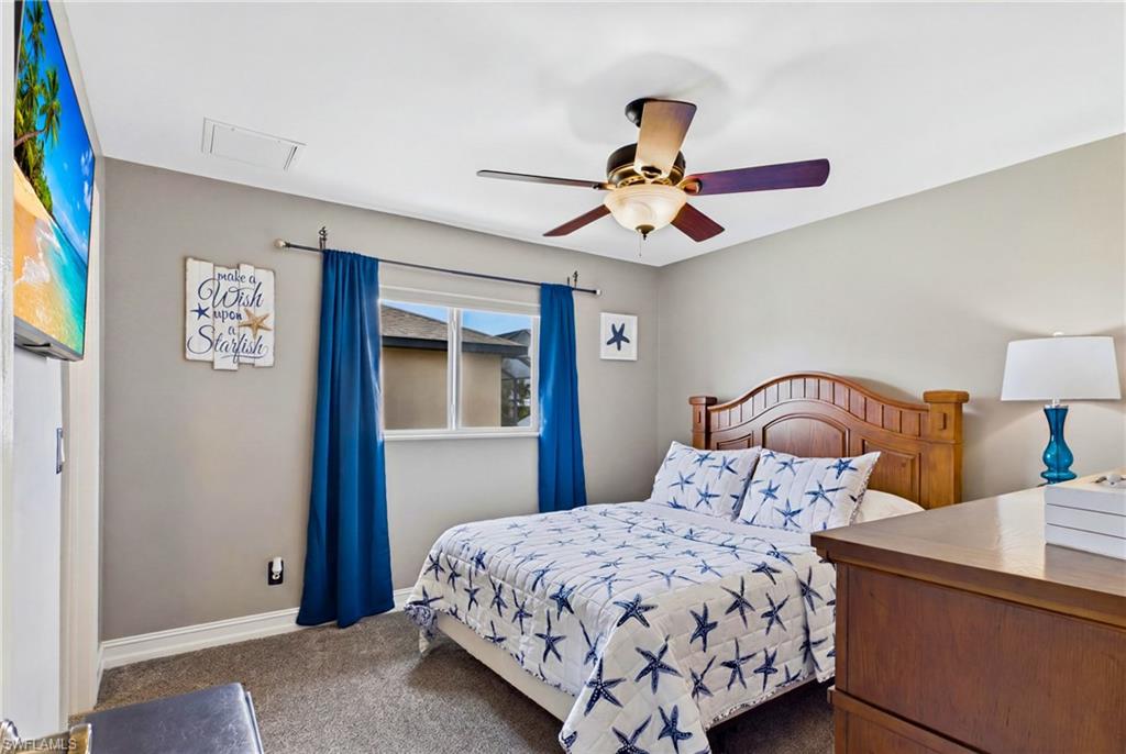 Bedroom featuring a window with blue drapes, ceiling fan with light fixture, light gray walls, and gray carpet flooring