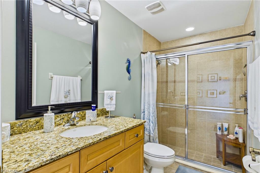 Bathroom featuring a single vanity with a granite countertop, light wood-finish cabinetry, an undermount sink, and a framed mirror