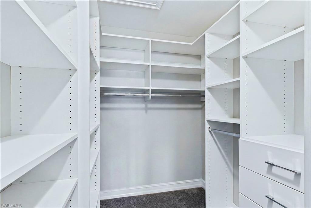 Walk-in closet featuring white built-in shelving, multiple hanging rods, and integrated drawers with silver-tone hardware