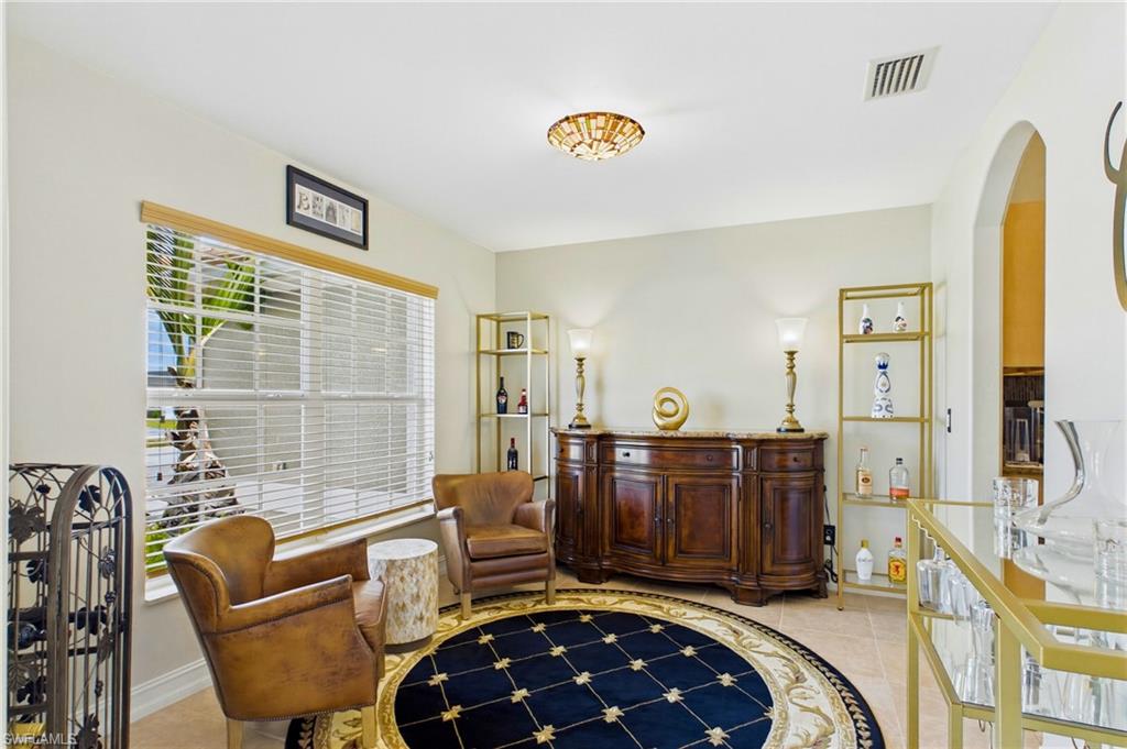 Spacious room featuring a large window with horizontal blinds, arched entryway, tile flooring, and a decorative ceiling light fixture