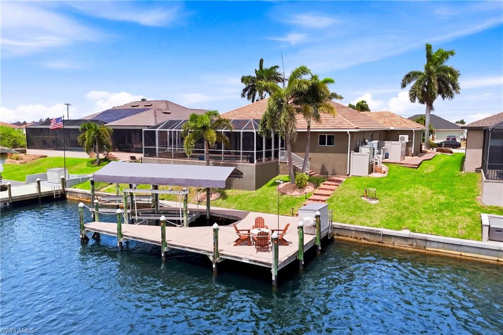Waterfront property featuring a private boat dock with covered lift, a screened lanai, mature palm trees, and a terraced lawn