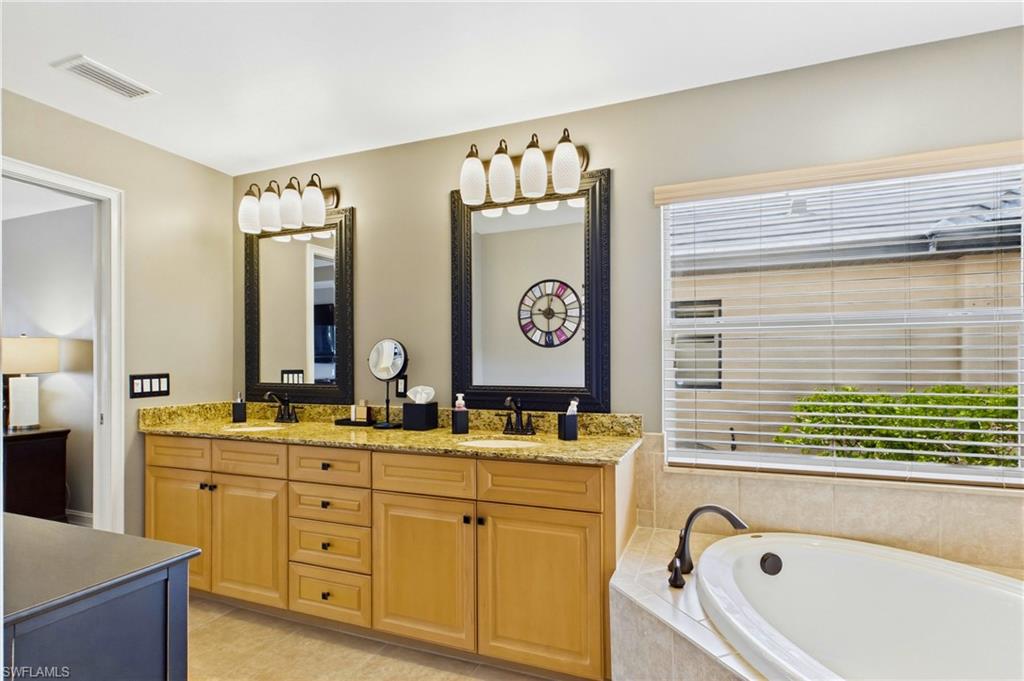 Double vanity featuring light wood cabinetry, stone countertops, and individual framed mirrors with integrated lighting