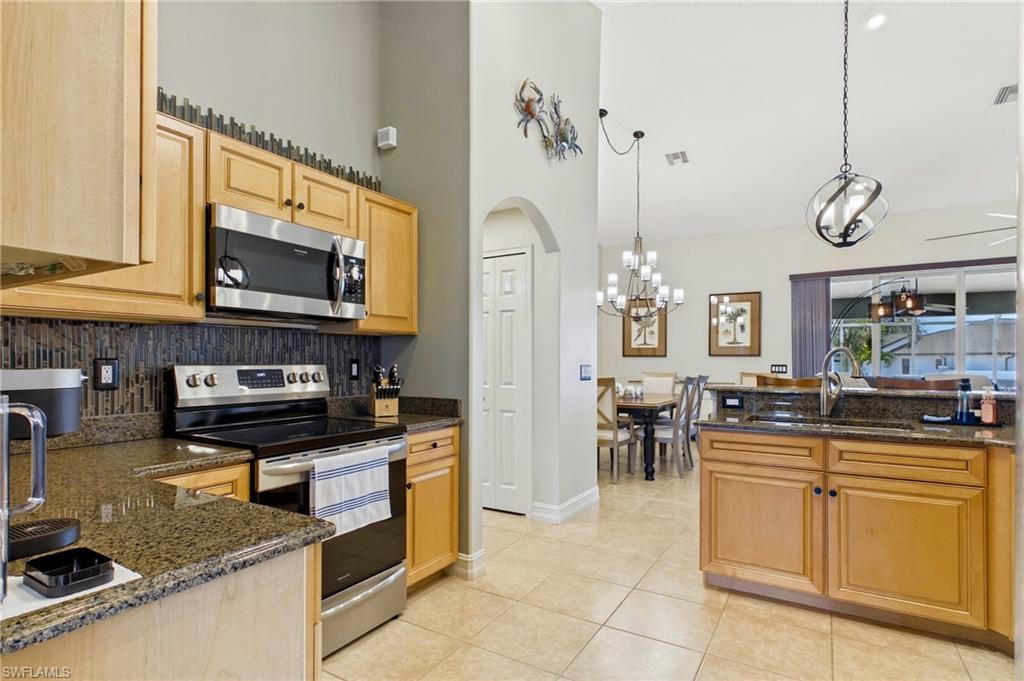 Kitchen featuring light wood cabinetry, stainless steel appliances, granite countertops, and a full-height tile backsplash