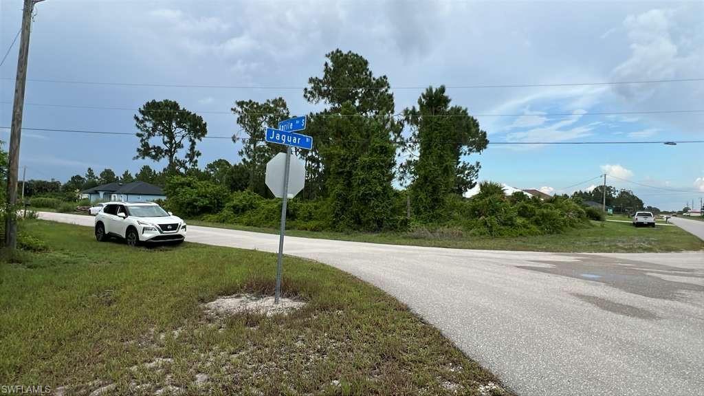 Corner lot featuring a street sign, paved roads, and natural landscaping with mature trees