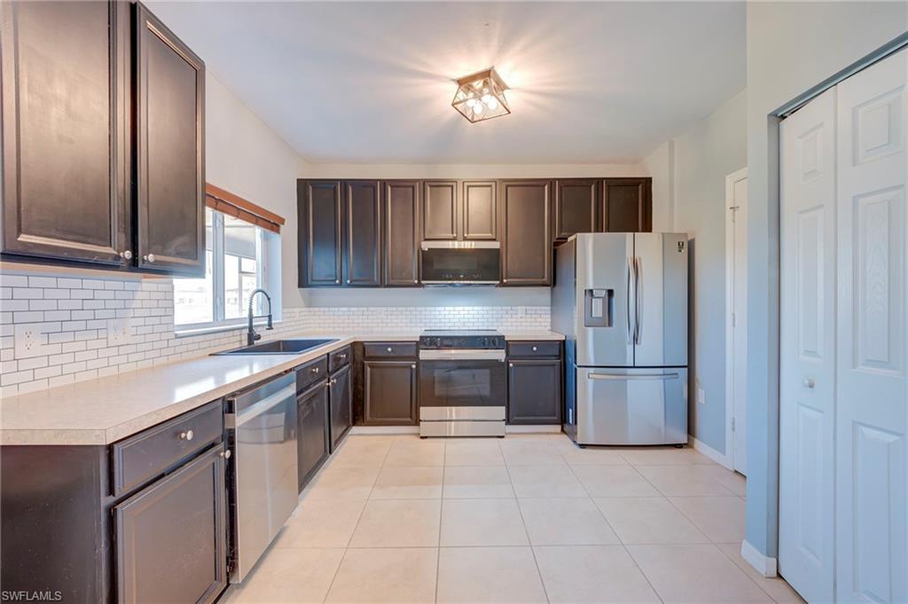 Kitchen featuring stainless steel appliances, light countertops, dark wood finish cabinets, and light tile patterned floors