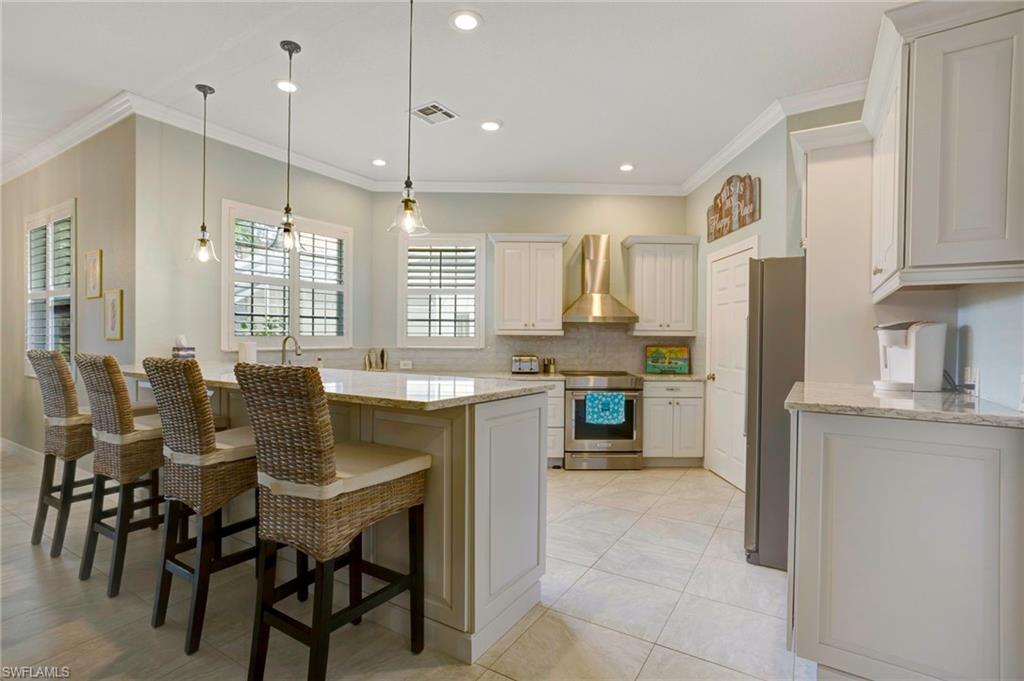 Kitchen featuring light stone countertops, appliances with stainless steel finishes, wall chimney range hood, and white cabinets