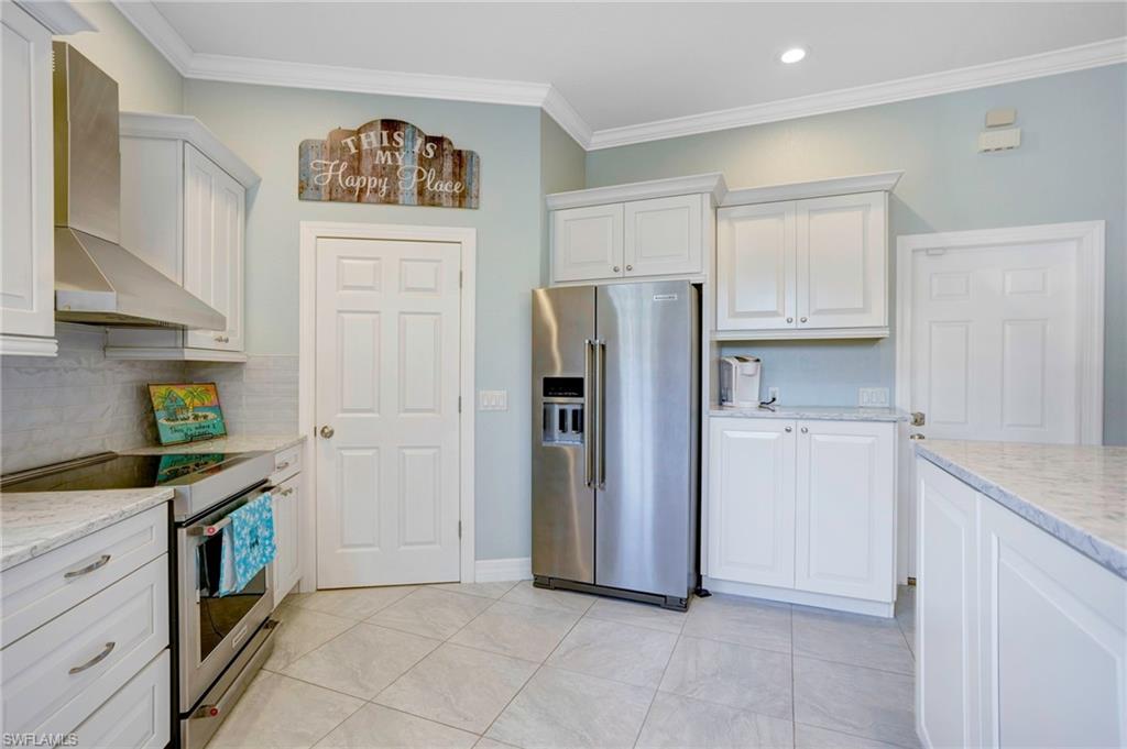Kitchen featuring wall chimney range hood, appliances with stainless steel finishes, white cabinetry, and ornamental molding