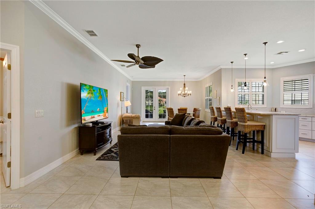 Tiled living room with sink, crown molding, and ceiling fan with notable chandelier