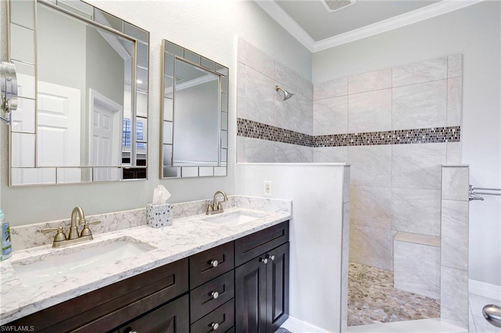 Bathroom featuring vanity, ornamental molding, and tiled shower