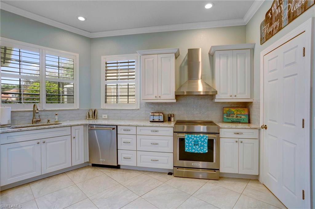 Kitchen with appliances with stainless steel finishes, white cabinetry, crown molding, wall chimney exhaust hood, and sink