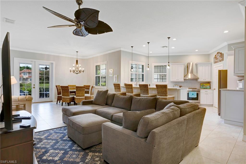 Living room with ornamental molding, a healthy amount of sunlight, ceiling fan with notable chandelier, and light tile patterned floors