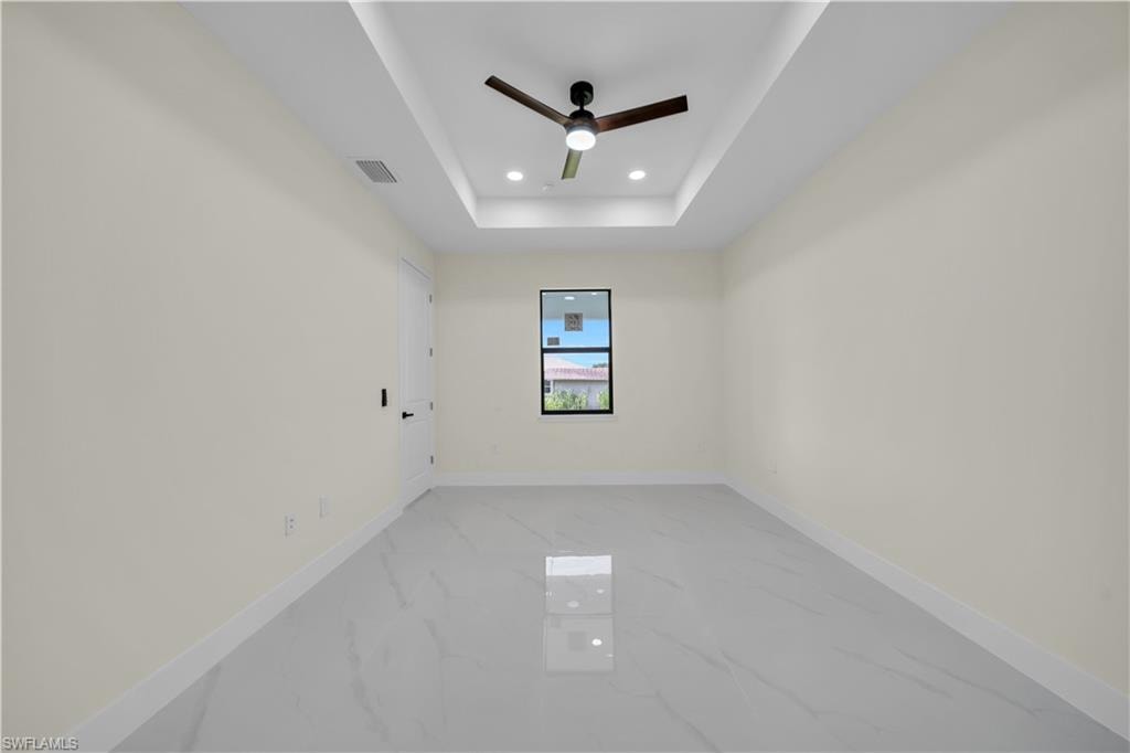 Spacious room featuring large format tile flooring, a tray ceiling with recessed lighting, and a modern ceiling fan