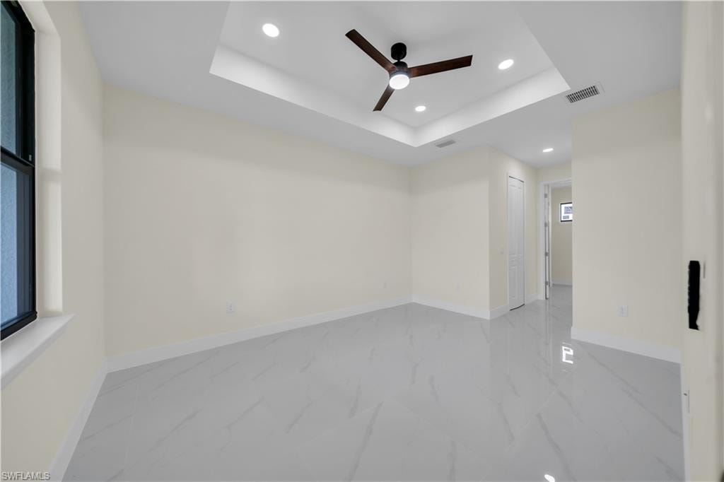 Spacious room featuring large format tile flooring, a tray ceiling, recessed lighting, a ceiling fan, and white baseboards