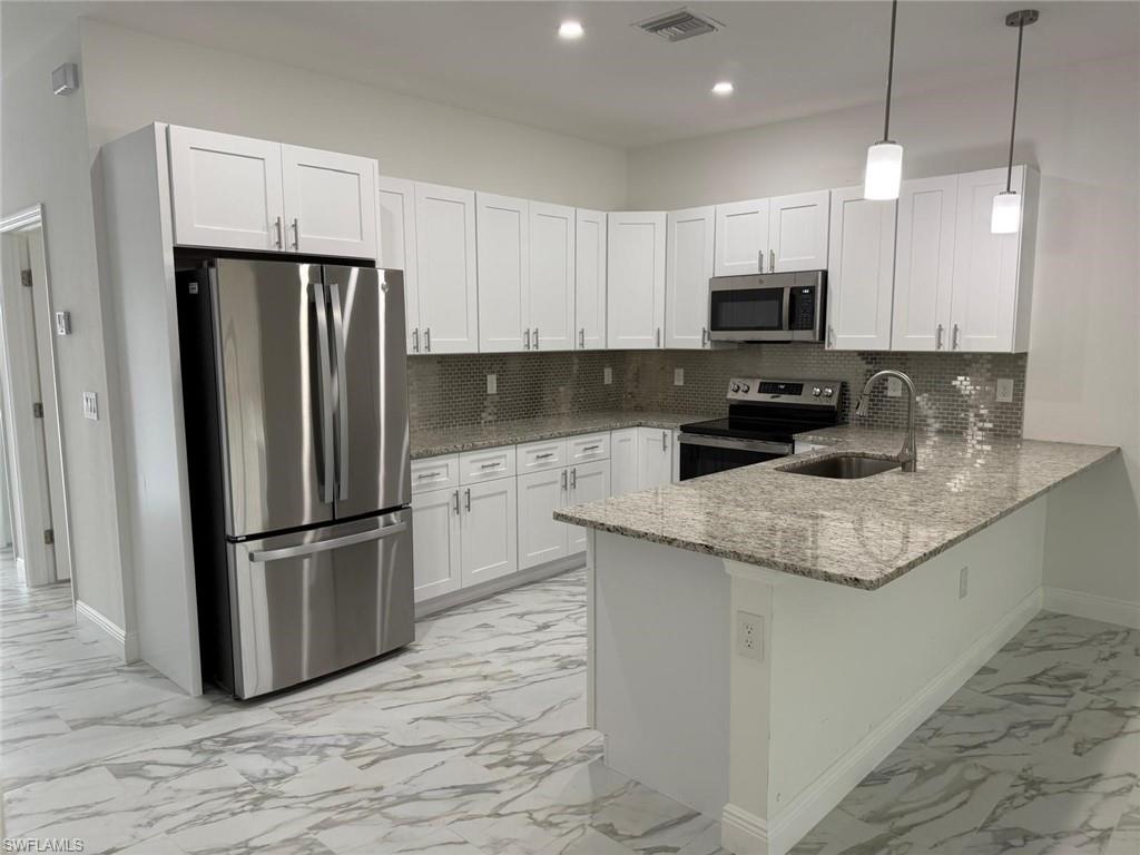Kitchen with stainless steel appliances, a sink, light marble finish floors, baseboards, and a peninsula