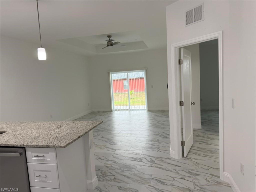 Kitchen with light marble finish flooring, a tray ceiling, a ceiling fan, baseboards, and white cabinets