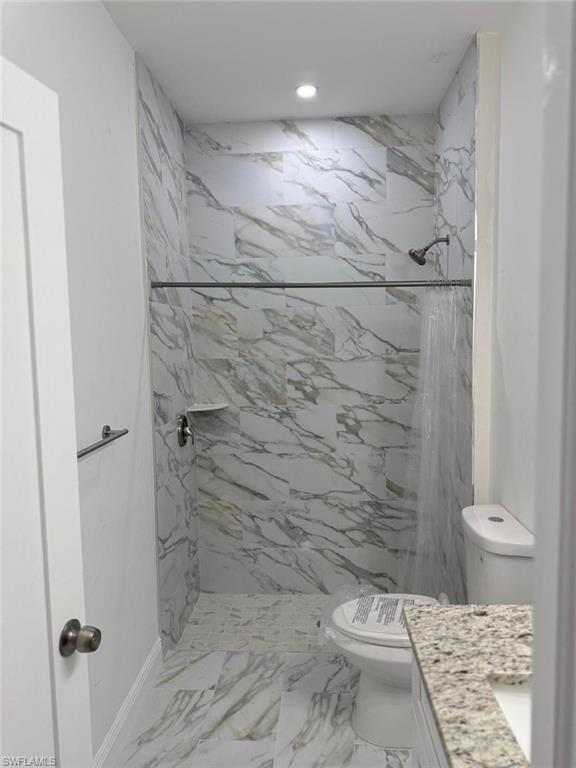 Bathroom with toilet, a marble finish shower, marble finish floors, vanity, and recessed lighting