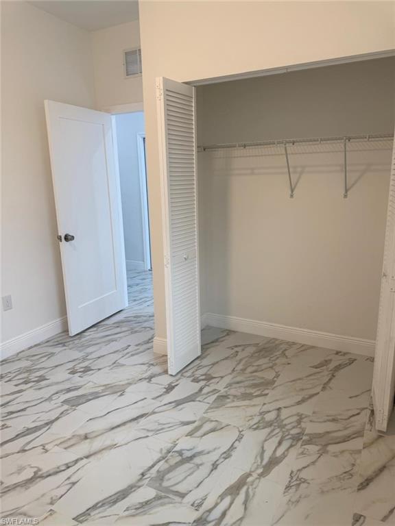 Unfurnished bedroom with light marble finish floors, a closet, and baseboards