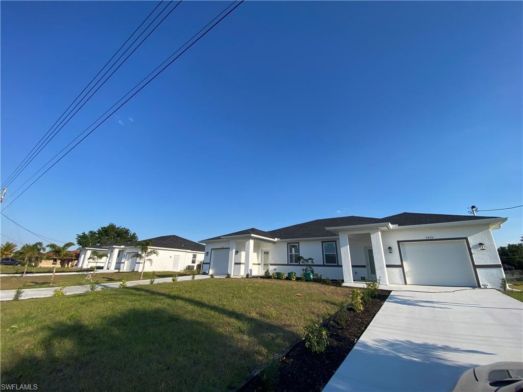 View of front of property featuring a front yard, driveway, a garage, and stucco siding