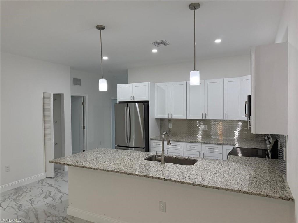 Kitchen with stainless steel appliances, a sink, a peninsula, light stone counters, and recessed lighting