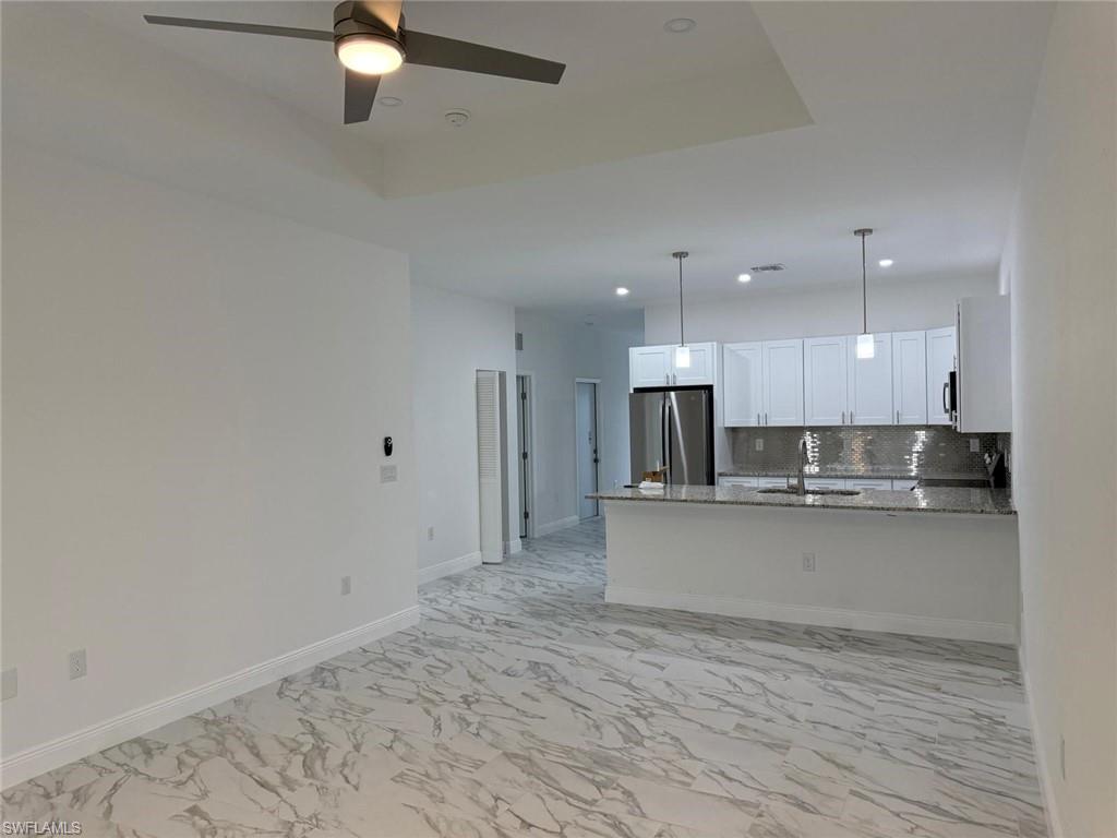 Kitchen featuring appliances with stainless steel finishes, a ceiling fan, white cabinetry, light marble finish flooring, and a peninsula