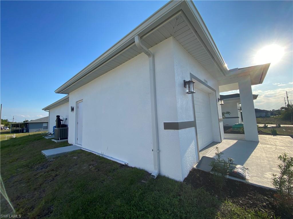 View of side of home with concrete driveway, central air condition unit, stucco siding, a yard, and a garage