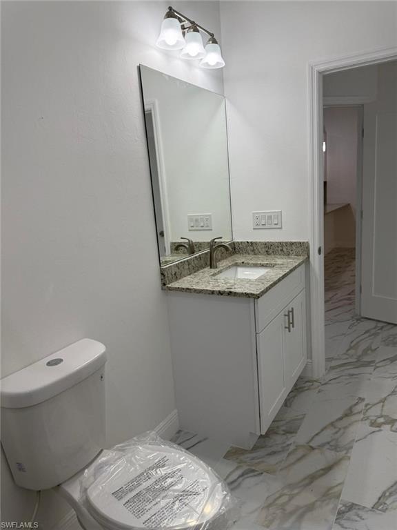 Half bathroom featuring marble finish flooring, toilet, and vanity