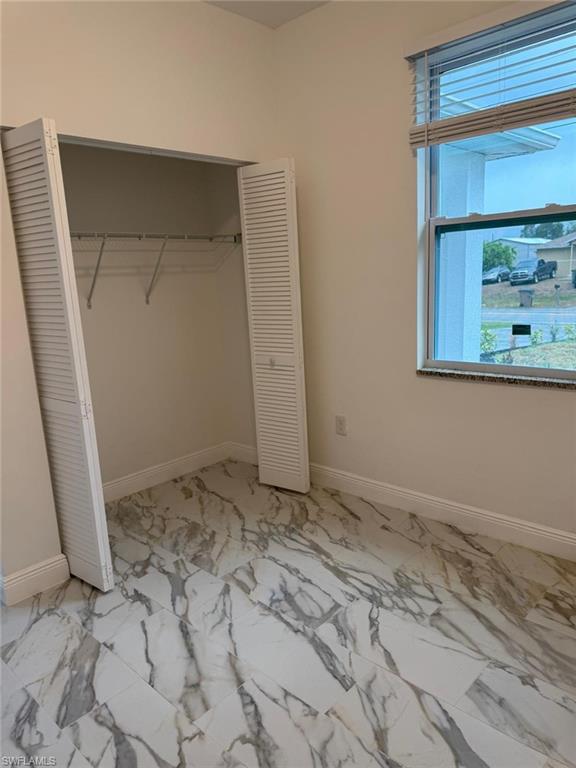 Unfurnished bedroom with a closet, multiple windows, marble look tiles, and baseboards