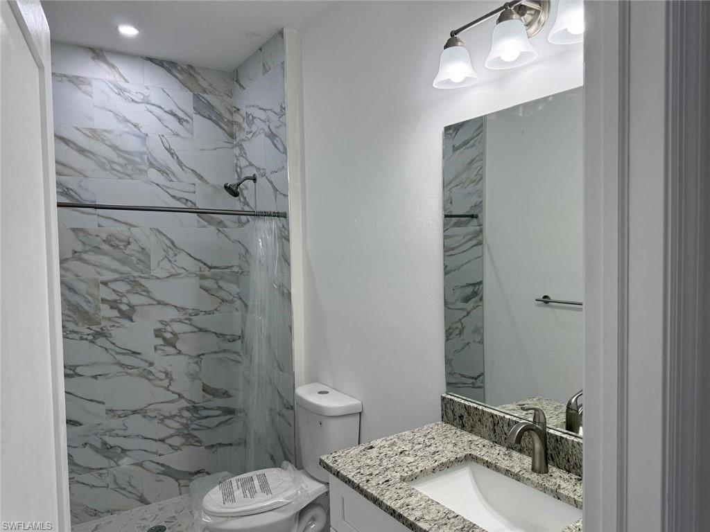 Full bathroom with toilet, vanity, and a marble finish shower