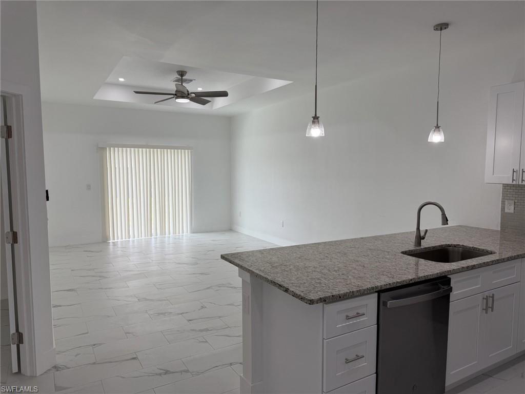 Kitchen featuring a sink, dishwashing machine, a tray ceiling, ceiling fan, and light marble finish floors