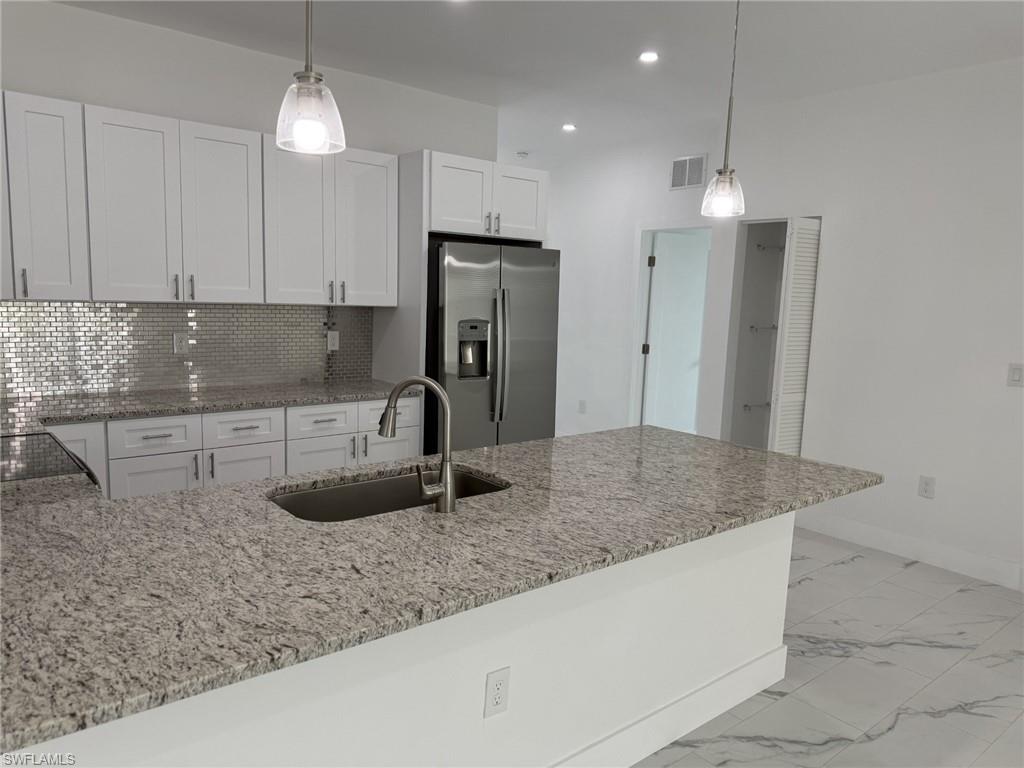 Kitchen featuring stainless steel fridge with ice dispenser, a sink, white cabinetry, light stone countertops, and recessed lighting