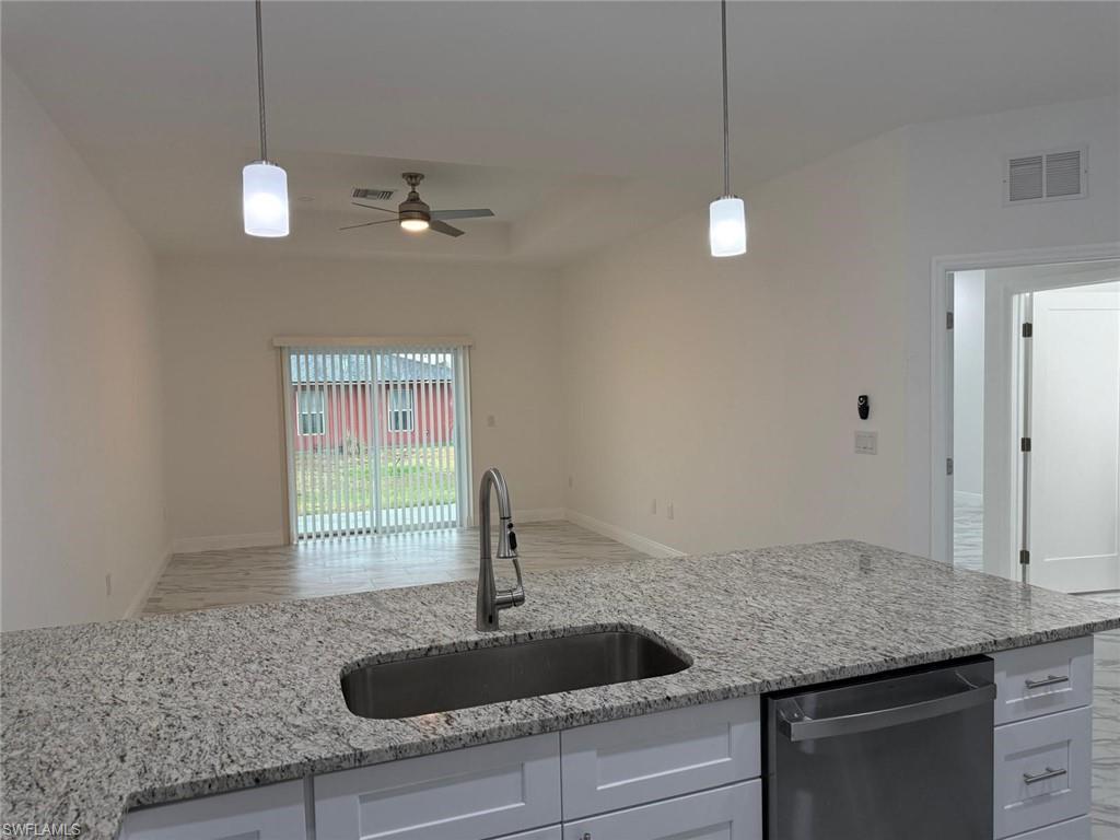 Kitchen featuring stainless steel dishwasher, a sink, a ceiling fan, open floor plan, and light stone countertops