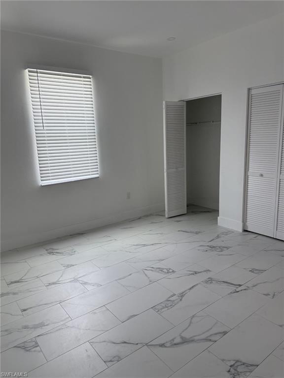 Unfurnished bedroom with light marble finish flooring, multiple closets, and baseboards