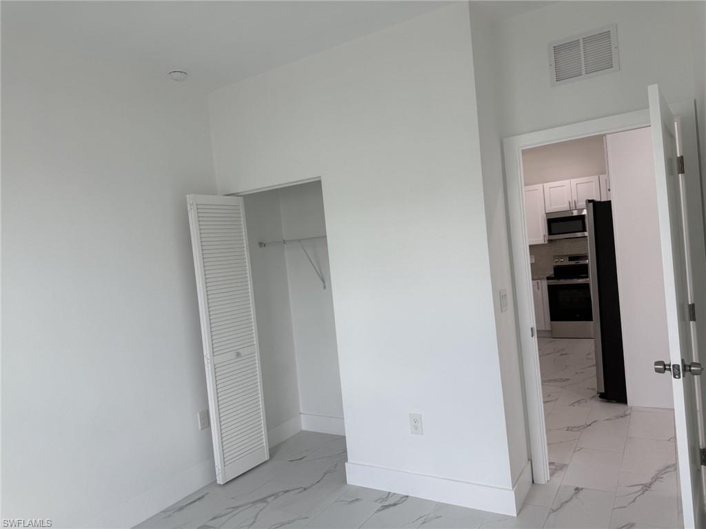 Unfurnished bedroom with light marble finish flooring, freestanding refrigerator, baseboards, and a closet