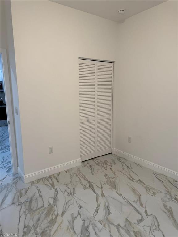 Unfurnished bedroom with light marble finish floors, baseboards, and a closet