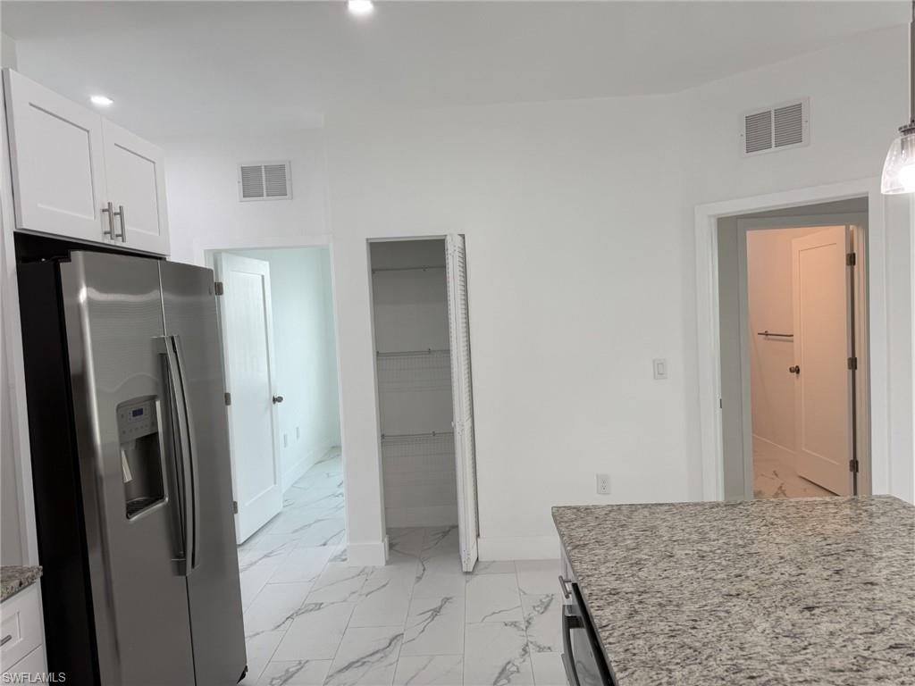 Kitchen with stainless steel refrigerator with ice dispenser, light marble finish flooring, white cabinetry, recessed lighting, and light stone counters