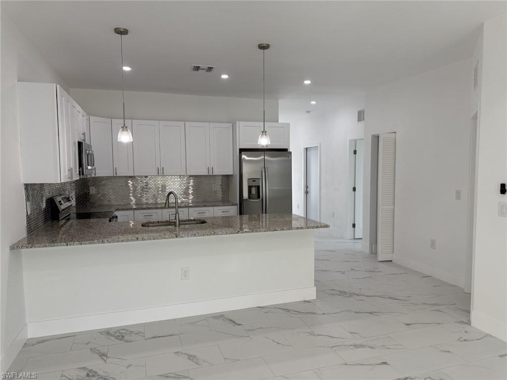 Kitchen with appliances with stainless steel finishes, a sink, a peninsula, baseboards, and stone counters