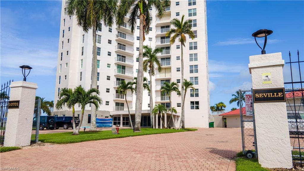 High-rise residential building featuring multiple balconies, a paver driveway, and mature palm trees