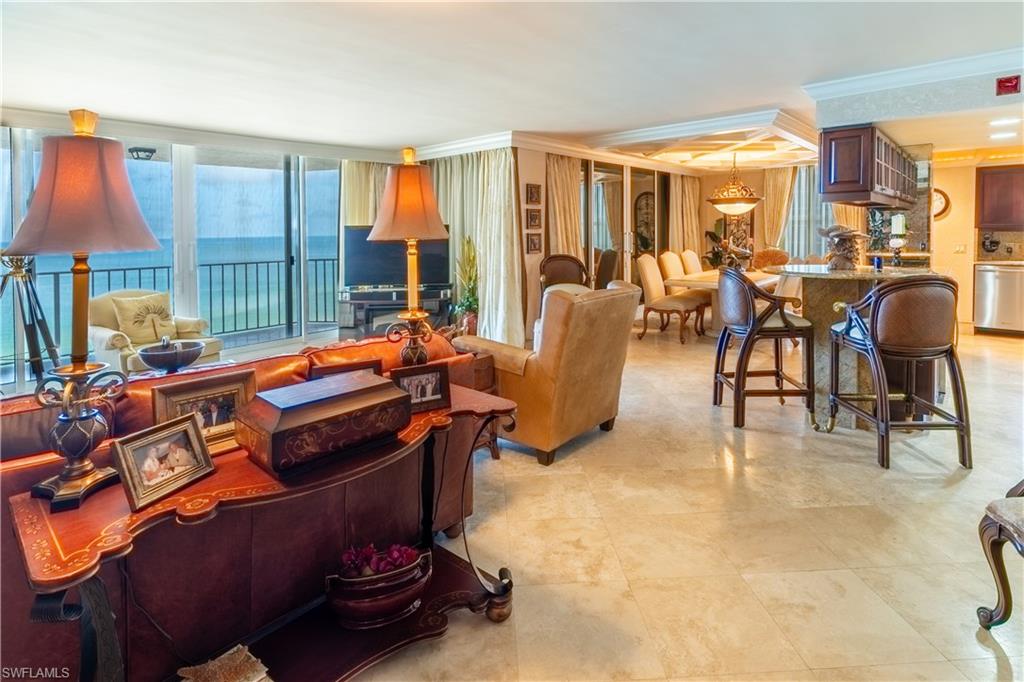 Open-concept living space featuring expansive glass doors, balcony access, large format tile flooring, a kitchen with dark wood cabinetry, and a tiered ceiling with recessed lighting