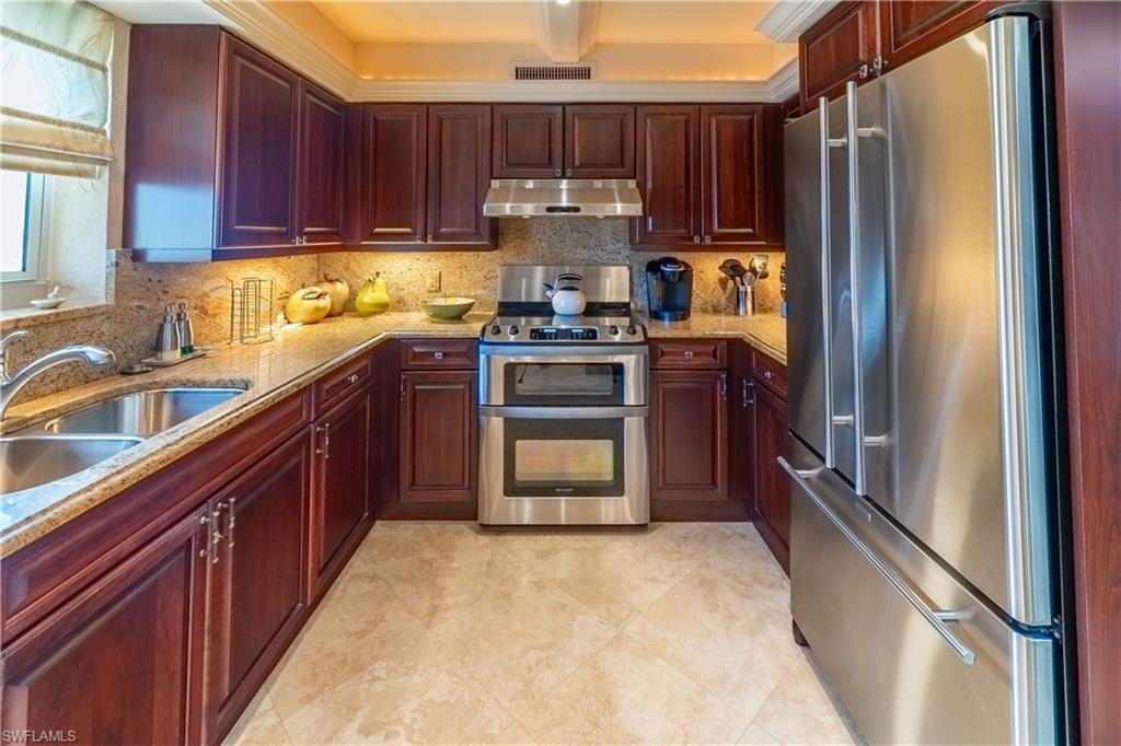 U-shaped kitchen featuring wood cabinetry, light-toned countertops, stainless steel appliances, and a double basin sink