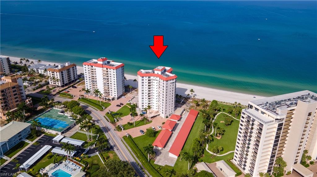 Coastal high-rise condominium featuring a white facade and red roof, situated directly on a sandy beach