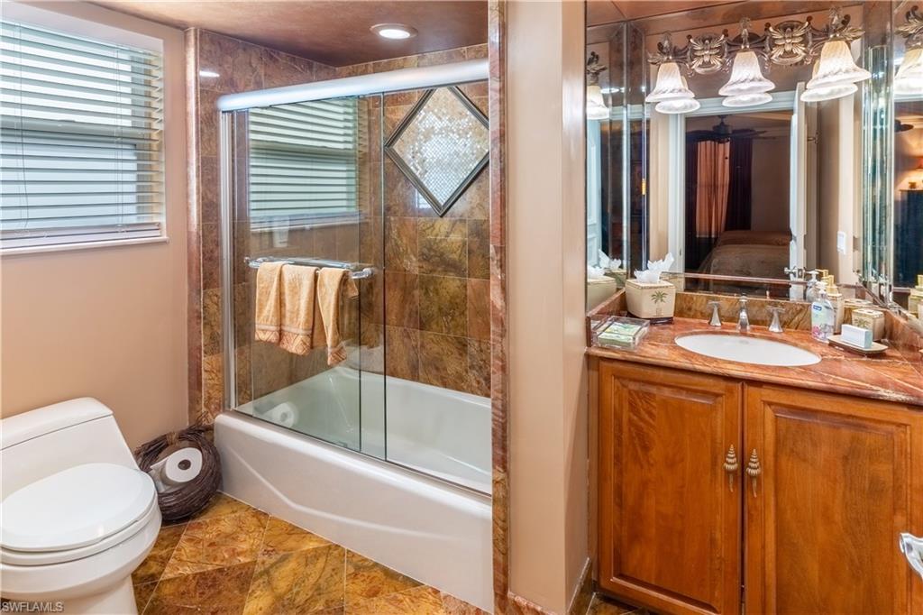 Bathroom featuring a wood vanity with a stone countertop, an integrated sink, and an extensive mirrored wall