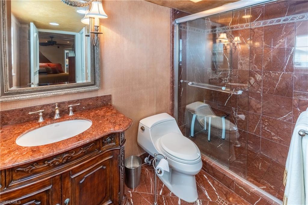 Bathroom featuring a glass-enclosed shower, a vanity with a red marble countertop and undermount sink, and ornate wood cabinetry