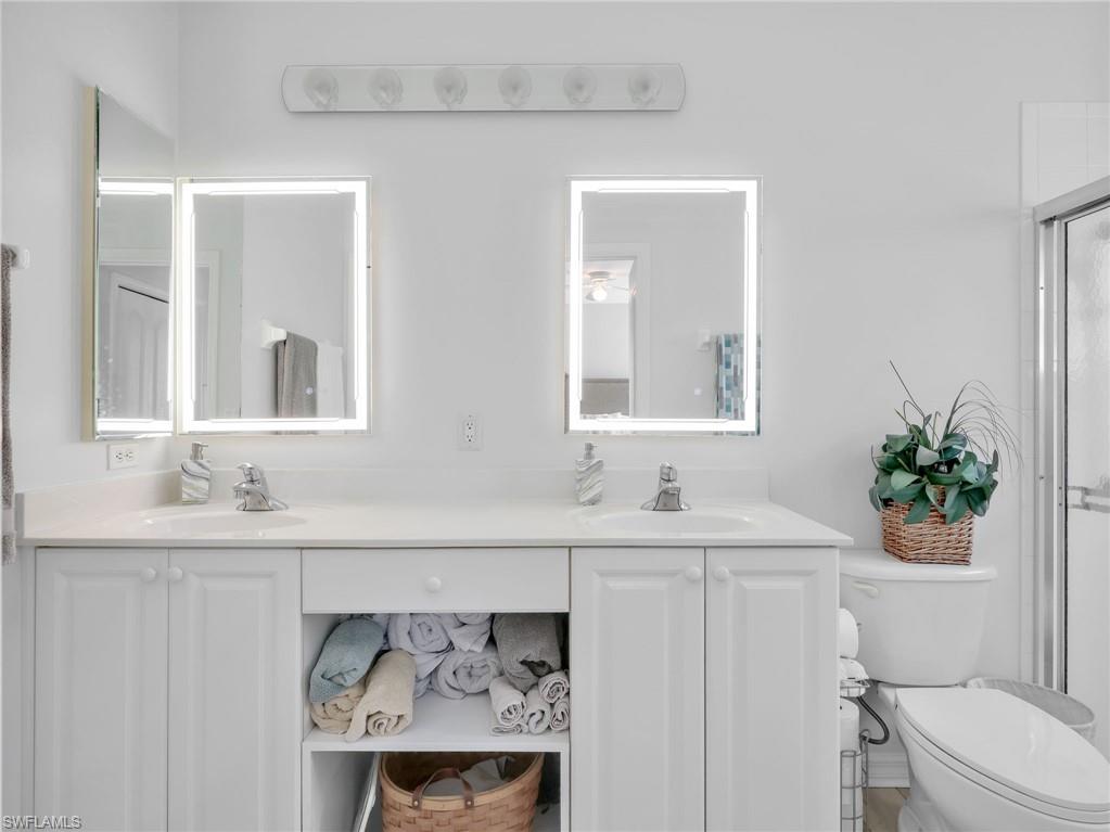 Dual vanity featuring white cabinetry, integrated sinks, chrome faucets, and illuminated mirrors