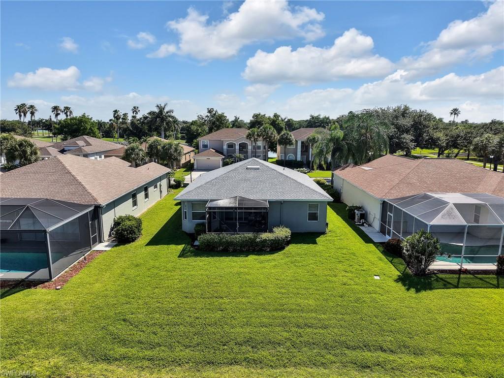 Rear exterior featuring a screened-in lanai, expansive green lawn, and mature landscaping