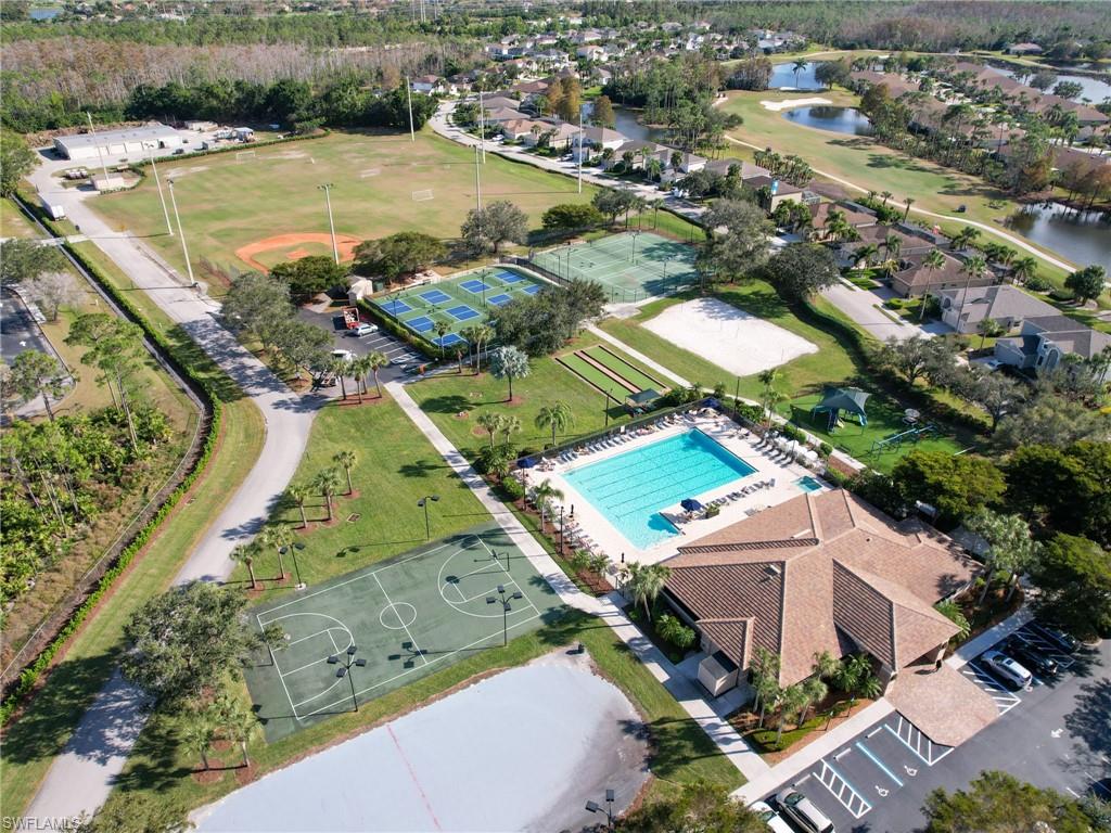 Aerial perspective showcasing community amenities including a large swimming pool, multi-court sports complex, multiple tennis courts, and a sand volleyball court