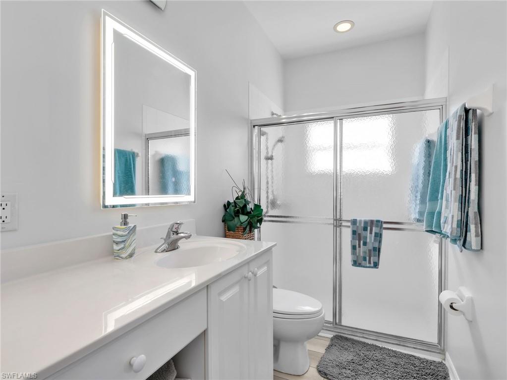 Bathroom featuring a white vanity with an integrated sink, a backlit rectangular mirror, a glass-enclosed shower with frosted panels, and recessed ceiling lighting