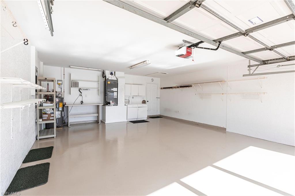 Garage featuring a garage door opener, electric water heater with circulating pump (extra one included!), and a/c - so much room! Pull down stairs to attic. Garage has extra roof tiles stacked on the side, attic has extra interior tiles stacked for easy reach. BTW- New Tile ROOF 2024!